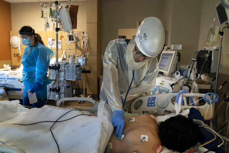 A medical worker in full protective equipment cares for a COVID-19 patient lying face down in a hospital bed.